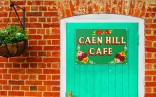 A bright green wooden door with a sign saying 'Caen Hill Cafe' written in traditional boat sign writing with canal roses.