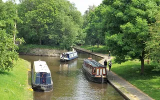 A boat passes two moored narrowboats on a sunny day