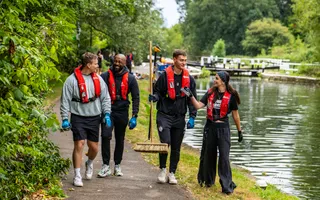 4 young adults walking on towpath, volunteering. All wearing life jackets, one holding a broom