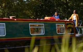 Two adults steer a narrowboat on a sunny day