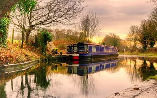 A narrowboat moors on the offside of the canal with the sunset reflecting on the water