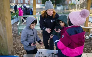 Volunteer working with children, looking at materials in a tray