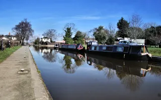 Wide shot of a canal on a sunny day with moored boats on the right
