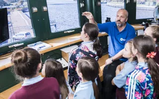 Group of school children inside a control room with adult show and telling