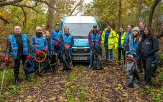 Group of volunteers pose in front of a branded van with litter pickers and bin bags in a wooded area.