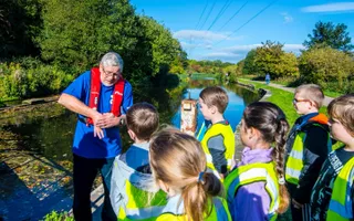 A Canal & River Trust worker stood next to the canal, explaining water safety to a group of school children