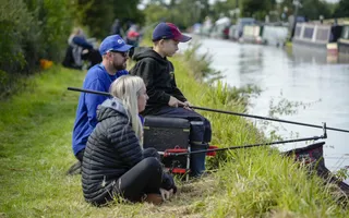 A fishing coach, sitting next to student learning how to fish.