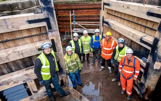 Group of Canal & River Trust workers in hard hats and high vis standing on the floor of a drained lock next to new lock gates