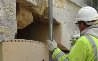 Employee in hi-vis and white hard-hat repairing stonework on bridge