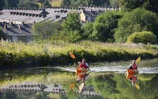 Two people paddle kayaks in the sun on the Leeds & Liverpool Canal