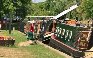 Two camping chair and a dog sit next to boats mooring nose to nose on a sunny stretch of the canal