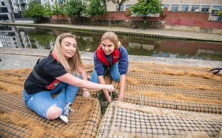 Two girls in life jackets smile as they plant floating reedbeds