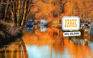 Boats moored along a canal with autumn trees either side and a Raffle graphic overlay