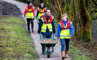 Youth volunteer group in the north west walking along a path with wheelbarrows