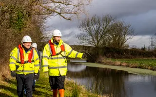 Two canal workers in high vis jackets walk along a towpath