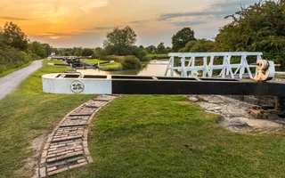 An orange sunset glows over a flat view of Caen Hill Locks, with a lock in the foreground and more further away.