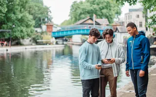 Three boys by the canal scrolling on their phones