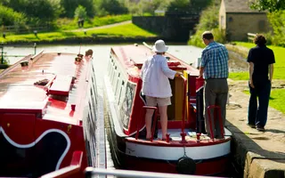 Two boats in a lock, one leaving, while people walk along the towpath