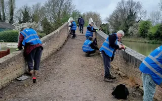 A group of people in blue hi vis vests tend to the walls of a bridge using hand held tools