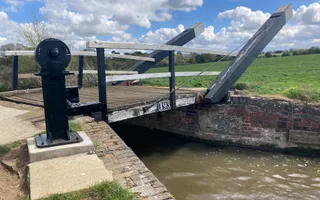 A bridge with a lock attached to it crosses over a small stretch of canal, with grass verges either side