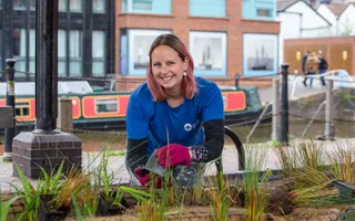 A woman wearing gloves smiles as she plants floating reedbeds next to the canal