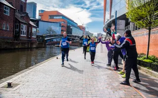Three fun runners jog along the towpath past crowds who are high-fiving them