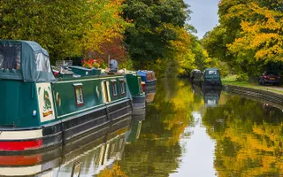 Boats moor along the Leeds & Liverpool Canal on an autumn day with trees reflected in the water