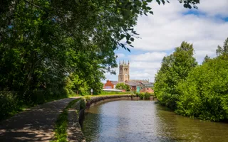 Canal turning to the right with green trees all around and a church in the distance