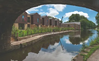 A row of houses and an old winch line the canal, with blue skies reflected in the water.