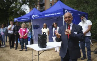 Man in a suit with a microphone giving a welcome speech in front of blue branded tents
