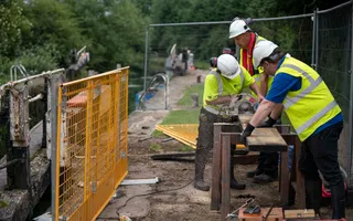Three canal workers cutting wood near a lock