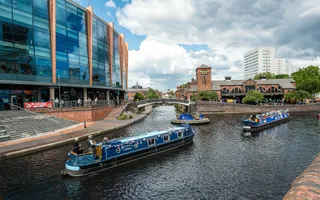 Three canals joining together with a mini roundabout in central Birmingham with two boats passing.