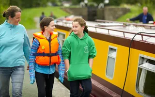 Three people walk along the towpath besides a moored hire boat