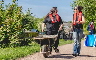 Two adults pushing a wheelbarrow along a towpath