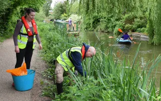 Canal & River Trust volunteers work in the bank while a narrowboat and kayak make use of the water
