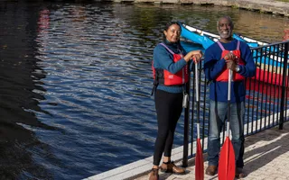 Two people with oars standing by the canal