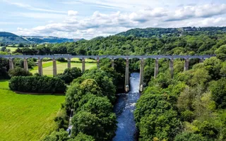 A dramatic aerial view of the Pontcysyllte Aqueduct, an impressively tall structure that passes high over a fast flowing river and green fields.