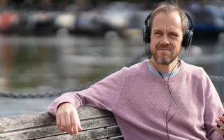 A person wearing headphones plugged into his phone sits on a bench in front of the canal.