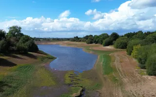 A dried up reservoir is surrounded by brown, dried grass and trees.