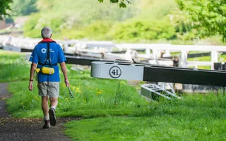 A Canal & River Trust volunteer with a windlass and lifejacket walking towards lock gates.